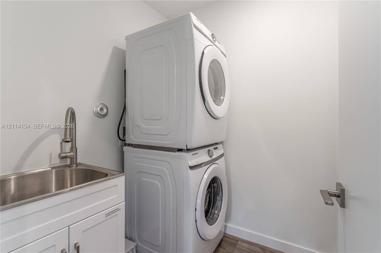 1126 NE 2nd Avenue, Fort Lauderdale, FL 33304 Stacked front-load laundry units with a white finish, stainless steel basin sink, and high-arc brushed nickel faucet set within a white cabinet vanity