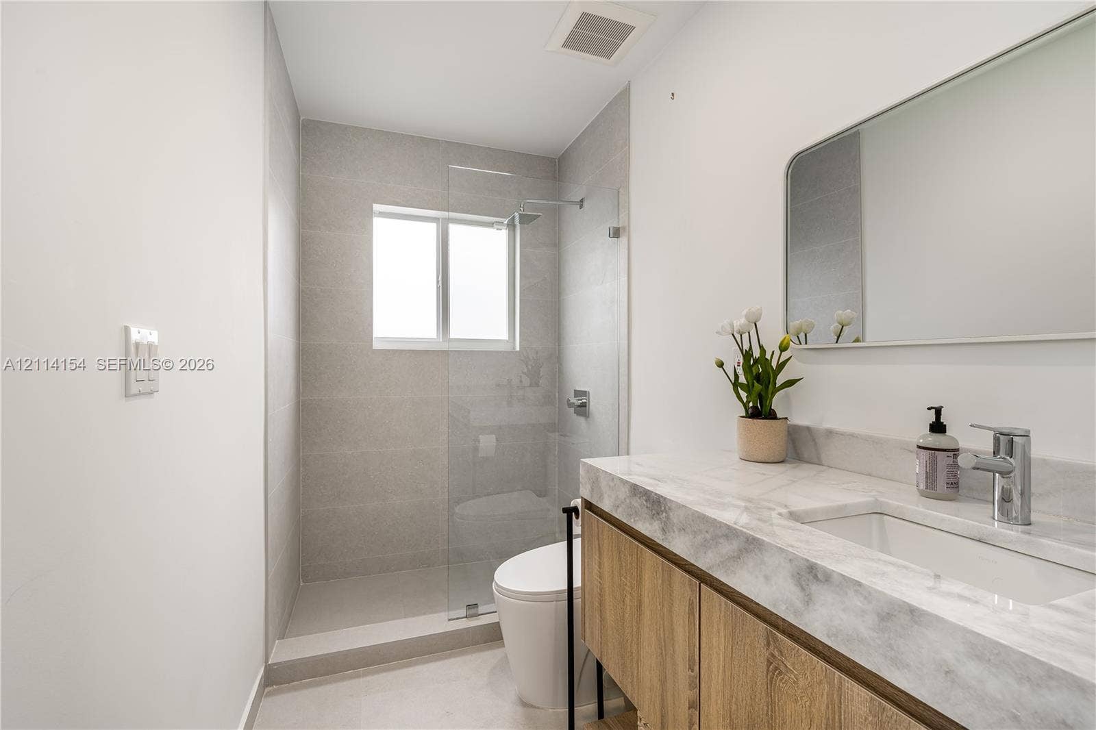 1126 NE 2nd Avenue, Fort Lauderdale, FL 33304 Bathroom featuring a floating wood-finish vanity, stone-topped integrated sink, glass-enclosed shower with full-height tile surround, and a wall-mounted rectangular mirror