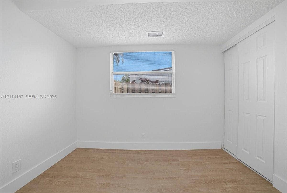2580 NW 62nd Avenue, Margate, FL 33063 Neutral-toned room featuring wood-finish flooring, a central window with horizontal blinds, and a built-in sliding-door closet