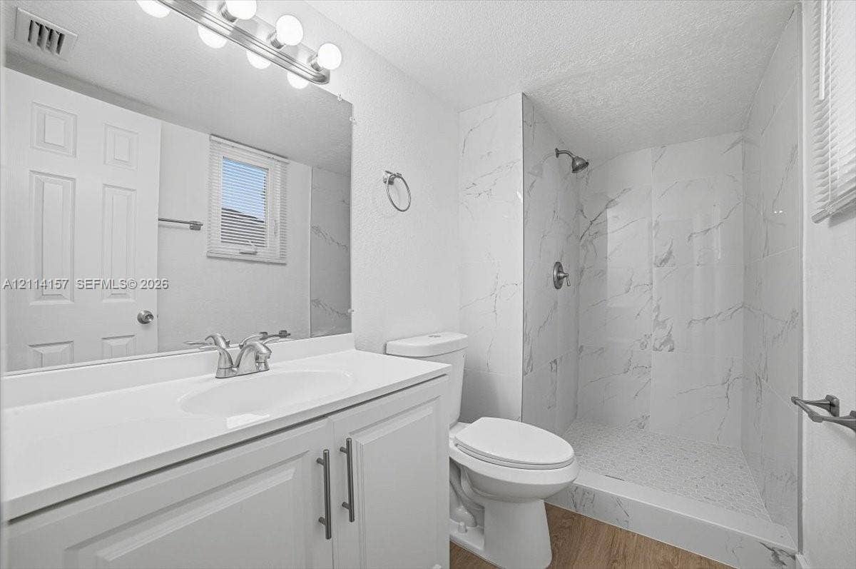 2580 NW 62nd Avenue, Margate, FL 33063 Bathroom featuring a white vanity with integrated sink, walk-in shower with floor-to-ceiling stone-pattern tile, polished chrome fixtures, and wood-finish flooring