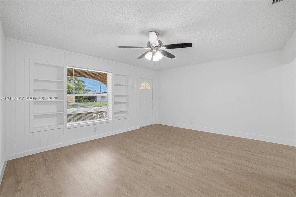 2580 NW 62nd Avenue, Margate, FL 33063 Interior space featuring wood-finish flooring, built-in shelving flanking a large window, a ceiling fan with integrated lighting, and a single-light panel entry door
