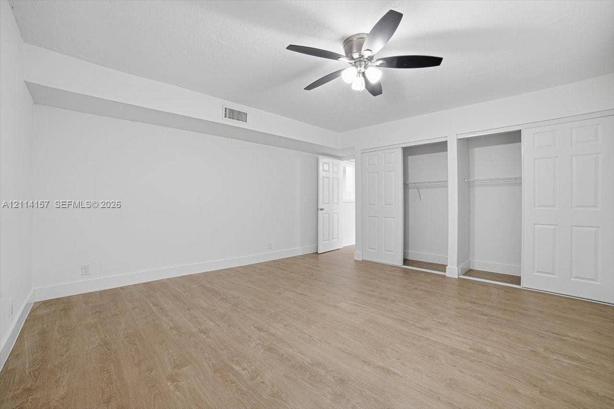 2580 NW 62nd Avenue, Margate, FL 33063 Room featuring wood-finish flooring, a multi-blade ceiling fan with integrated lighting, and dual closets with paneled sliding doors