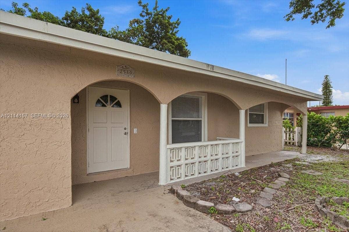 2580 NW 62nd Avenue, Margate, FL 33063 Stucco exterior featuring an arched covered porch, decorative concrete balustrade, and a solid door with arched glass inlay