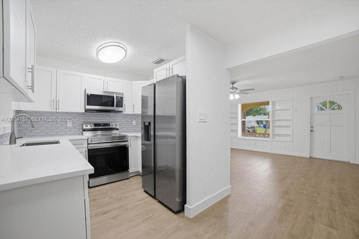 2580 NW 62nd Avenue, Margate, FL 33063 Kitchen featuring white cabinetry, stainless steel appliances, stone-look countertops, and a textured tile backsplash, complemented by wood-finish flooring