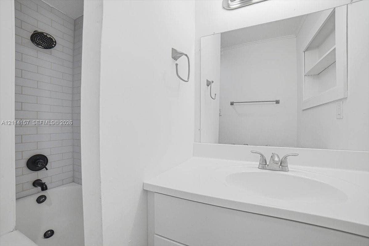 2580 NW 62nd Avenue, Margate, FL 33063 Bathroom featuring a white vanity with a composite countertop, subway tile shower surround, matte black shower fixtures, large rectangular vanity mirror, and built-in recessed shelving