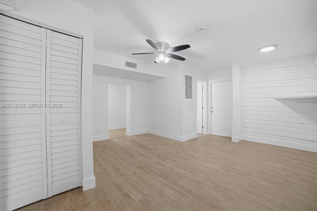 2580 NW 62nd Avenue, Margate, FL 33063 Interior space featuring wood-finish flooring, white shiplap accent wall, louvered bi-fold closet doors, and a ceiling fan with integrated lighting