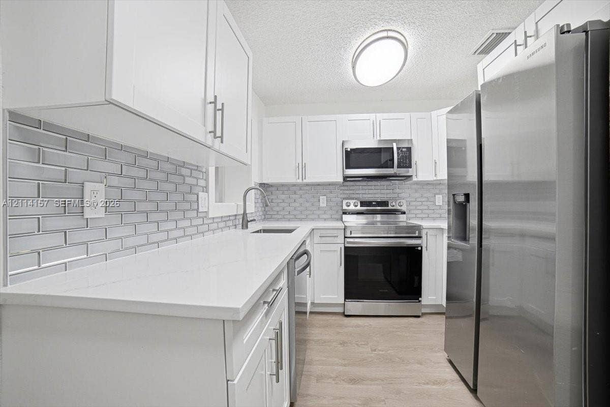 2580 NW 62nd Avenue, Margate, FL 33063 Kitchen featuring white shaker-style cabinetry, white solid-surface countertops, a gray subway tile backsplash, stainless steel appliances, and wood-finish flooring