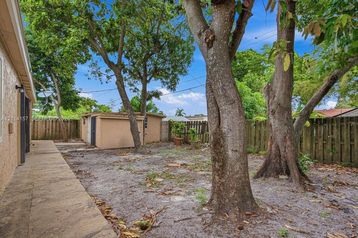 2580 NW 62nd Avenue, Margate, FL 33063 Rear yard featuring a concrete walkway, detached storage structure, and wood privacy fencing with mature trees