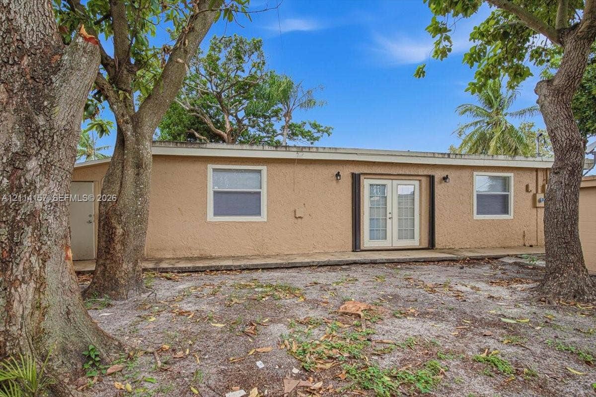 2580 NW 62nd Avenue, Margate, FL 33063 Stucco exterior featuring dual-pane windows, a central set of French doors, an exterior side entry door, and wall-mounted sconce lighting