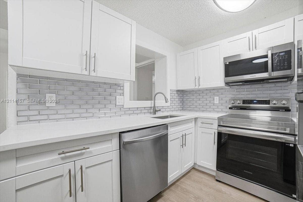2580 NW 62nd Avenue, Margate, FL 33063 Kitchen featuring white shaker-style cabinetry, stainless steel appliances, white solid-surface countertops, light grey subway tile backsplash, and wood-finish flooring