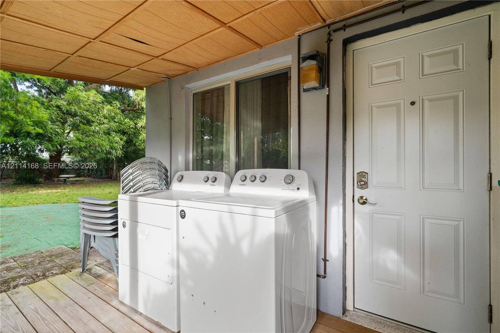 Covered exterior laundry area featuring wood-plank flooring, a paneled entry door with hardware