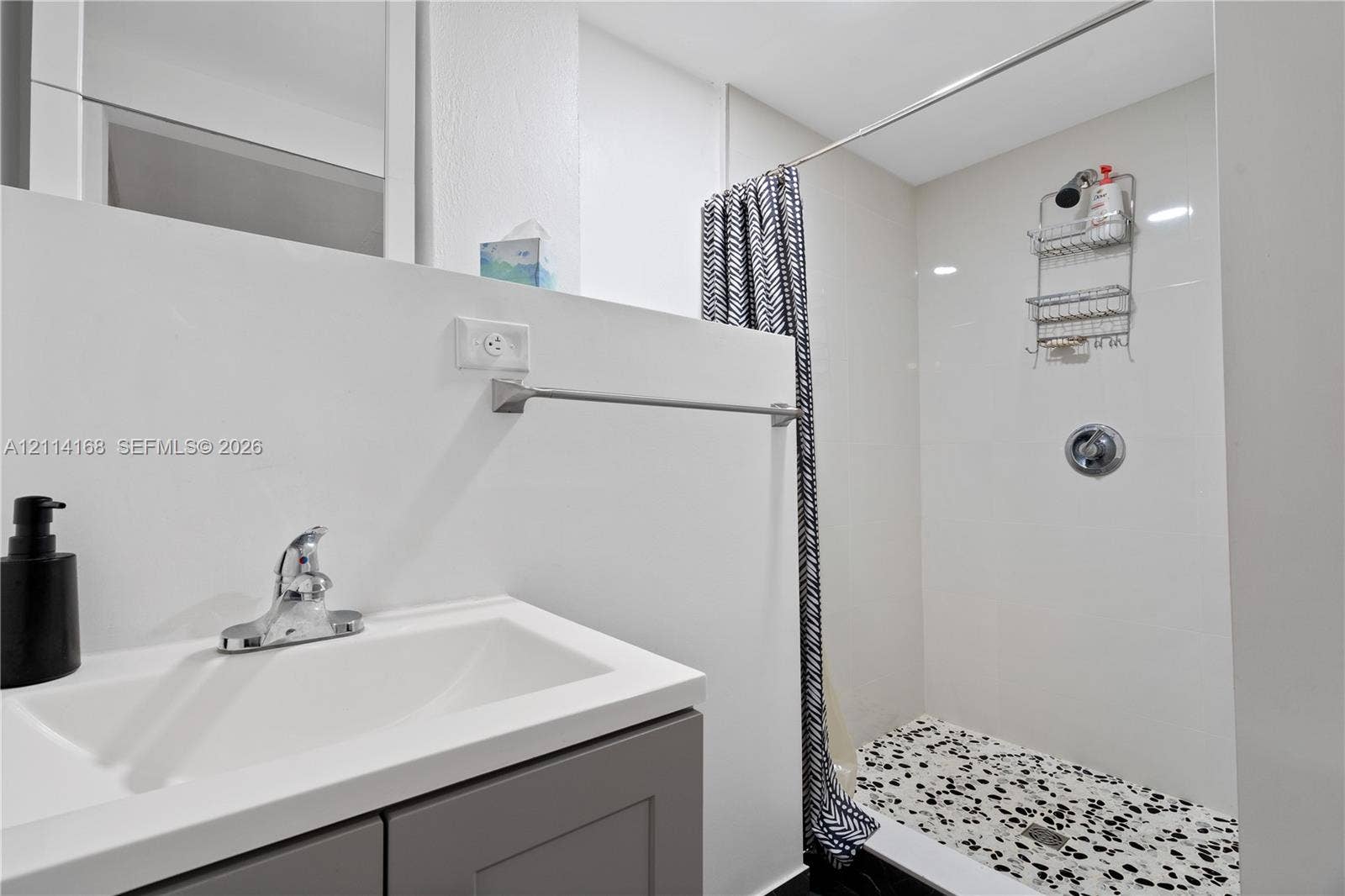 Bathroom featuring a gray vanity with a white countertop, polished chrome faucet, and a walk-in shower with white wall tile and a patterned floor (Flex space, in-law quarters)