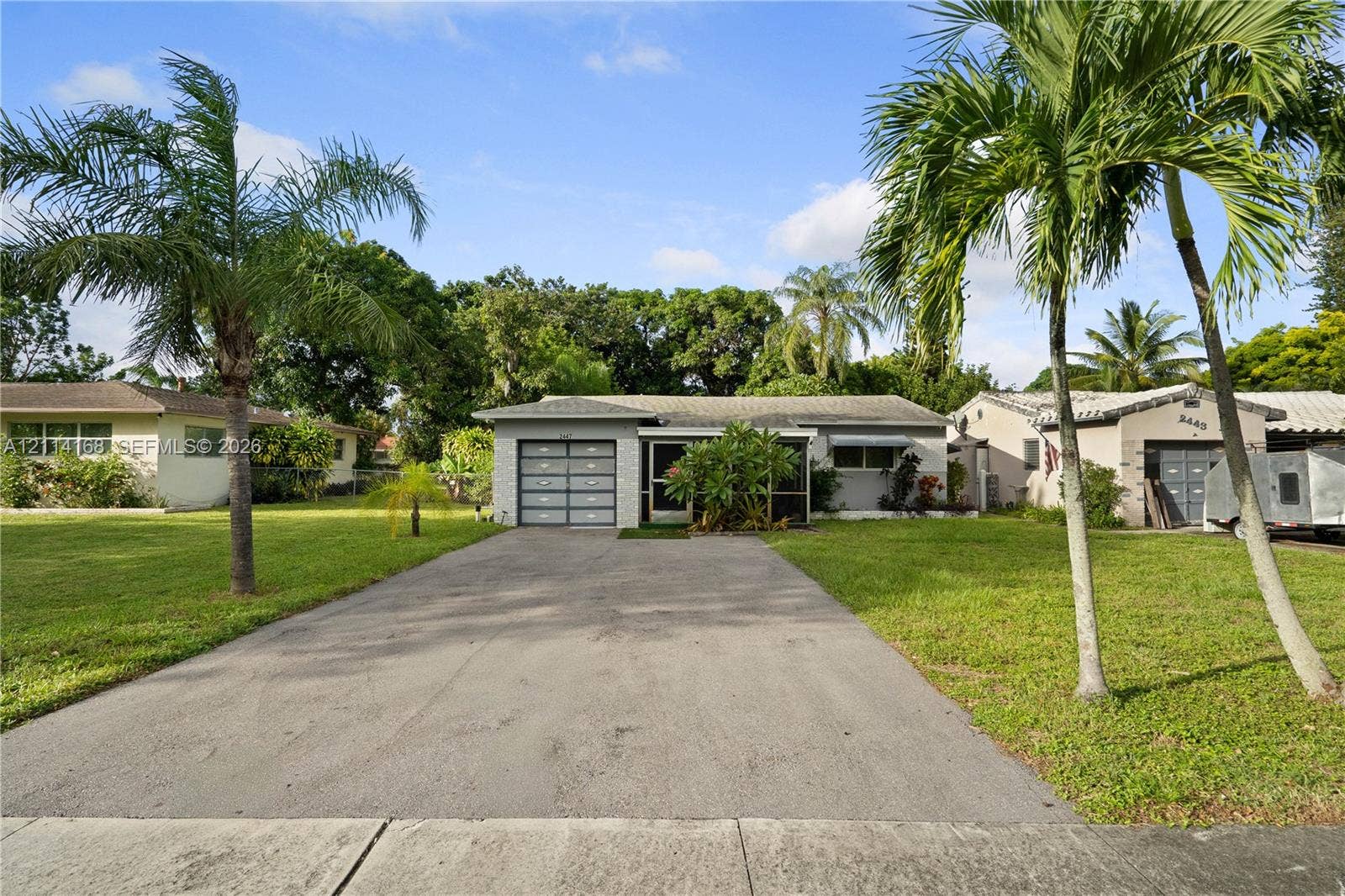 Single-story residence featuring a concrete driveway, with multi-panel garage door, and exterior landscaping including mature palm trees