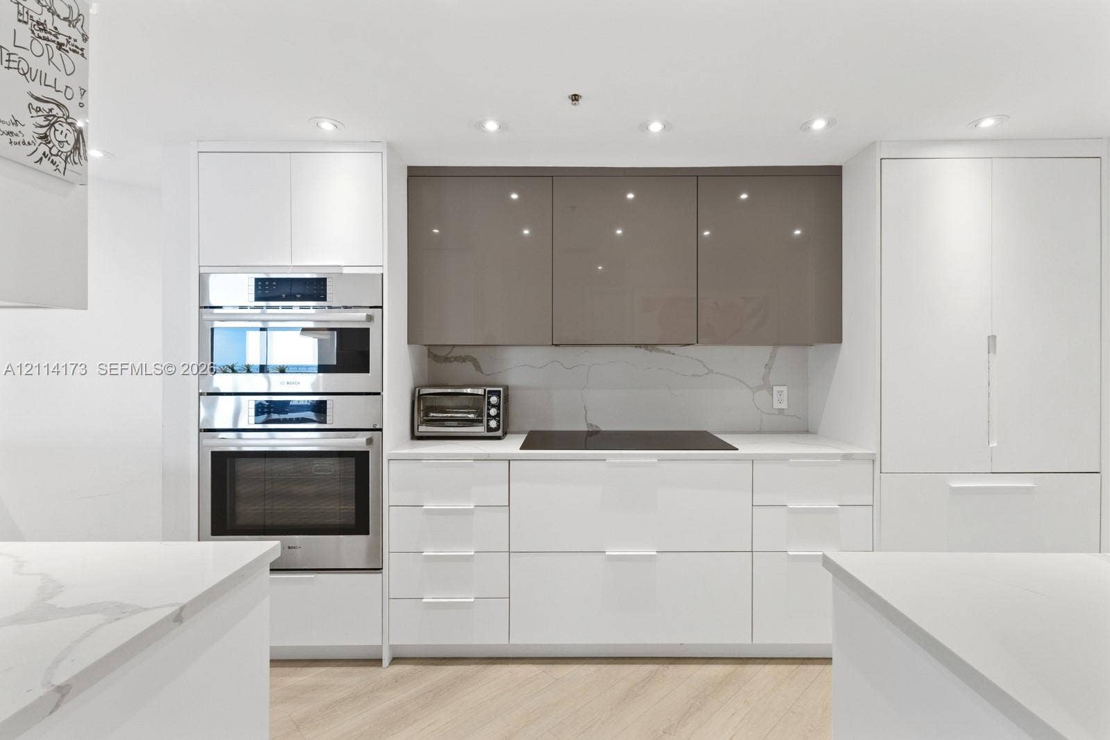 701 Brickell Key Boulevard, #1012, Miami, FL 33131 Modern kitchen featuring flat-panel high-gloss cabinetry, stone countertops with veining detail, integrated cooktop, built-in stainless steel double ovens, and wood-finish flooring