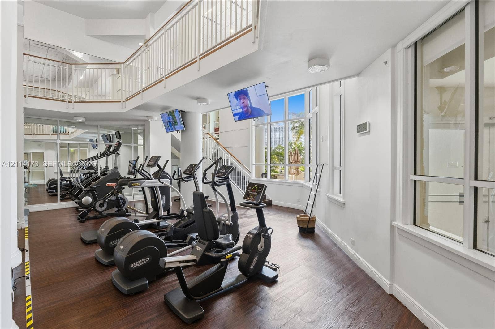701 Brickell Key Boulevard, #1012, Miami, FL 33131 Two-story fitness space featuring wood-finish flooring, floor-to-ceiling windows, an elevated mezzanine railing, and expansive mirrors