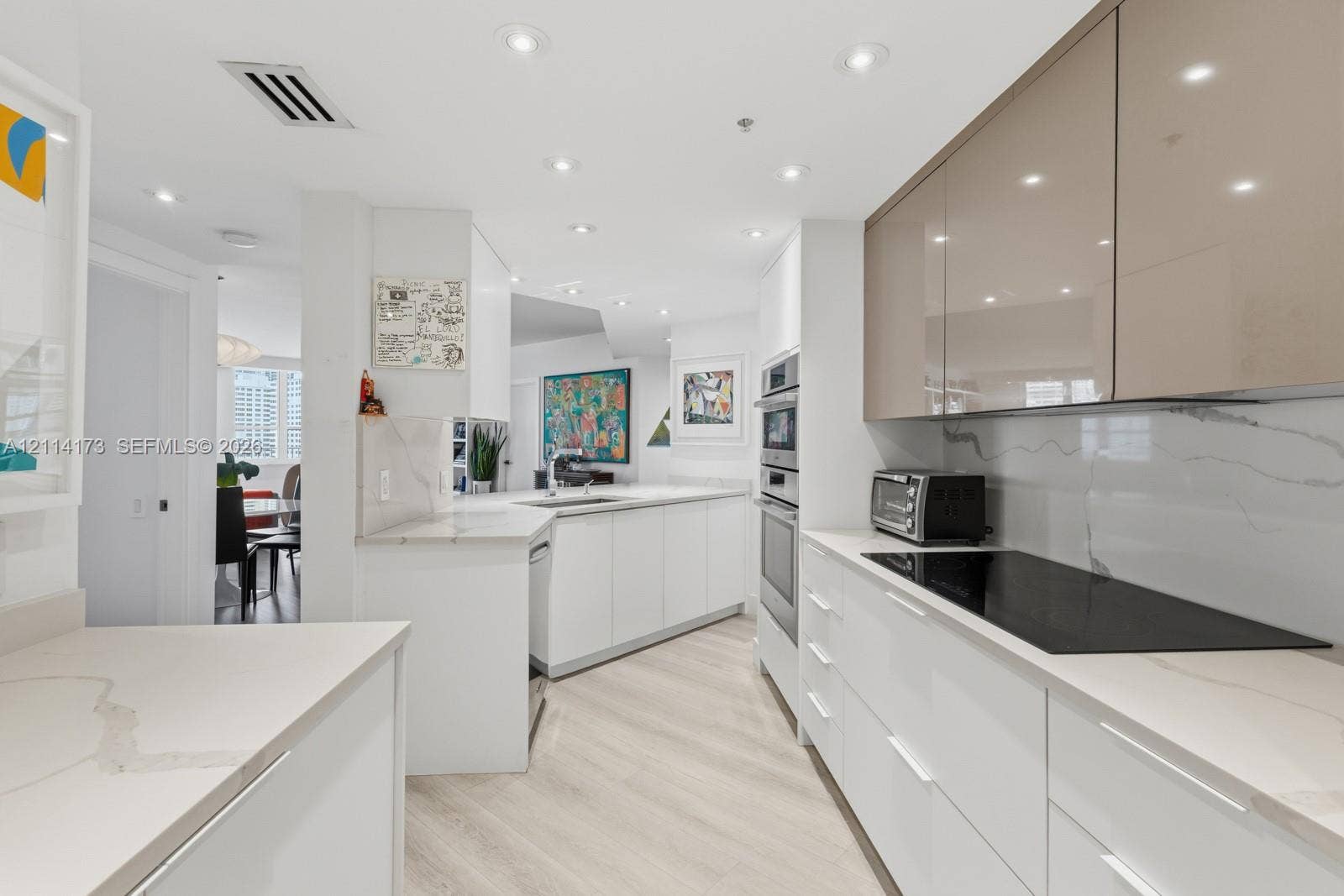 701 Brickell Key Boulevard, #1012, Miami, FL 33131 Modern kitchen featuring high-gloss white and metallic cabinetry, stone-finish countertops, full-height stone-finish backsplash, built-in wall oven, and recessed lighting