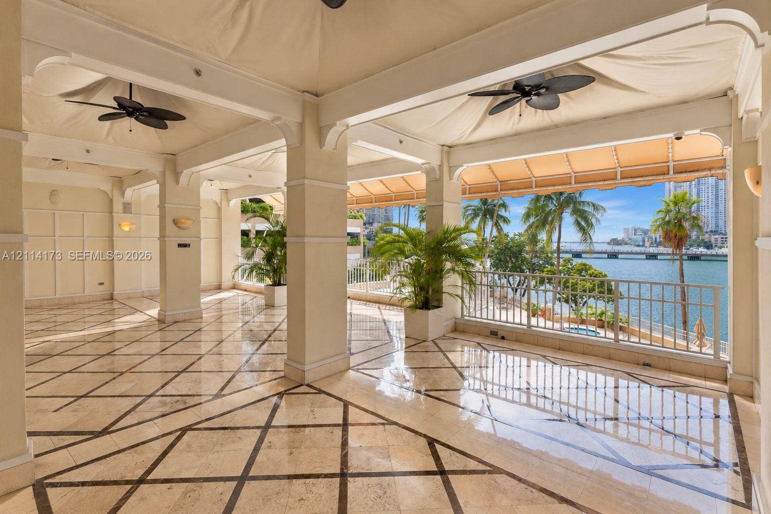 701 Brickell Key Boulevard, #1012, Miami, FL 33131 Covered terrace featuring stone tile flooring with decorative inlay, structural columns, ceiling-mounted fans, and metal railings overlooking the water