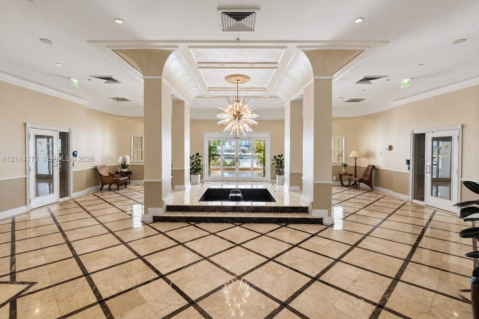 701 Brickell Key Boulevard, #1012, Miami, FL 33131 Grand lobby featuring polished stone flooring with geometric tile inlay, a central tiered water feature, soaring architectural pillars, recessed tray ceiling detailing, and an ornamental tiered light fixture