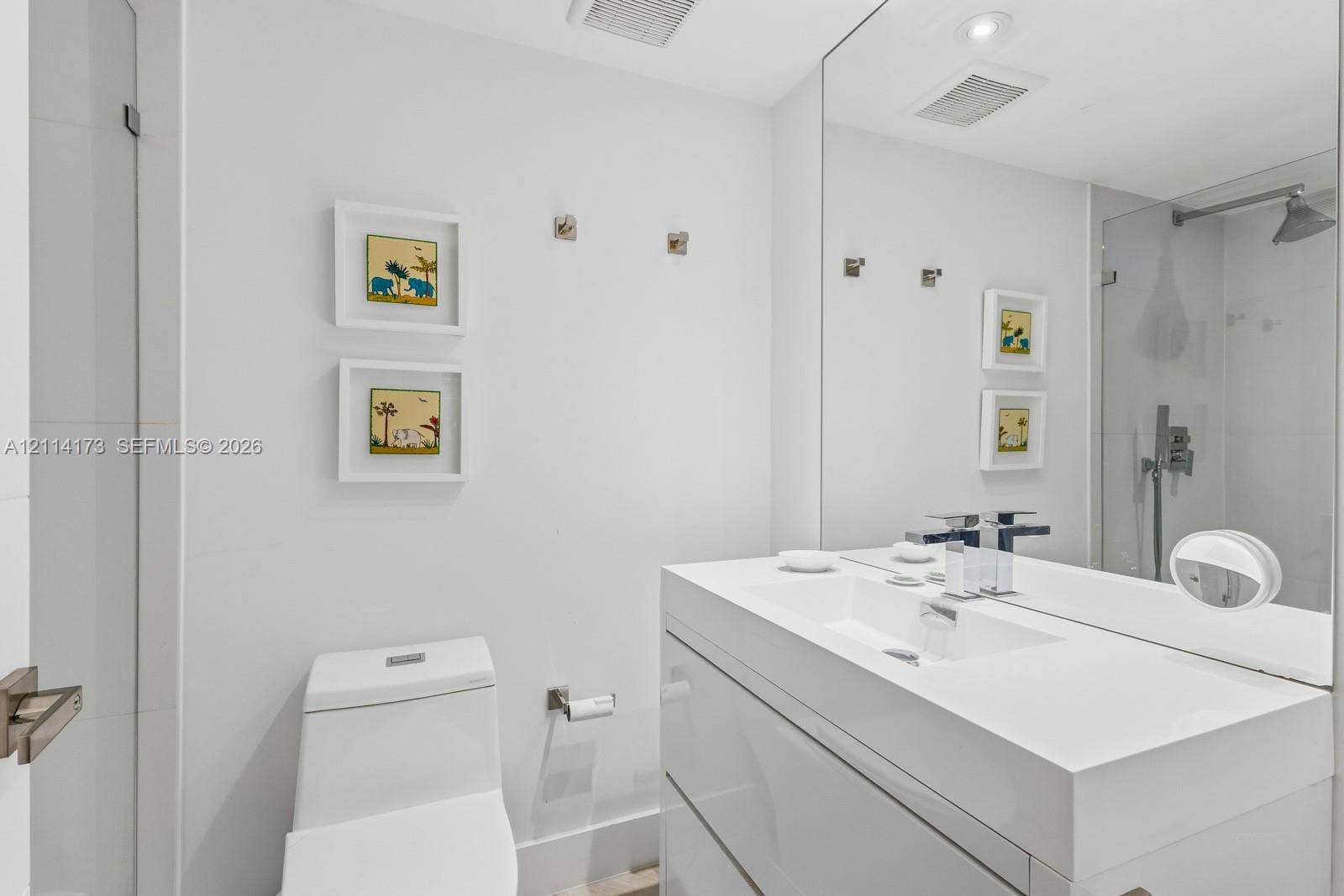 701 Brickell Key Boulevard, #1012, Miami, FL 33131 Modern floating vanity with a seamless integrated sink, polished chrome widespread faucet, large-format mirror, and glass-enclosed shower featuring a wall-mounted rainfall showerhead