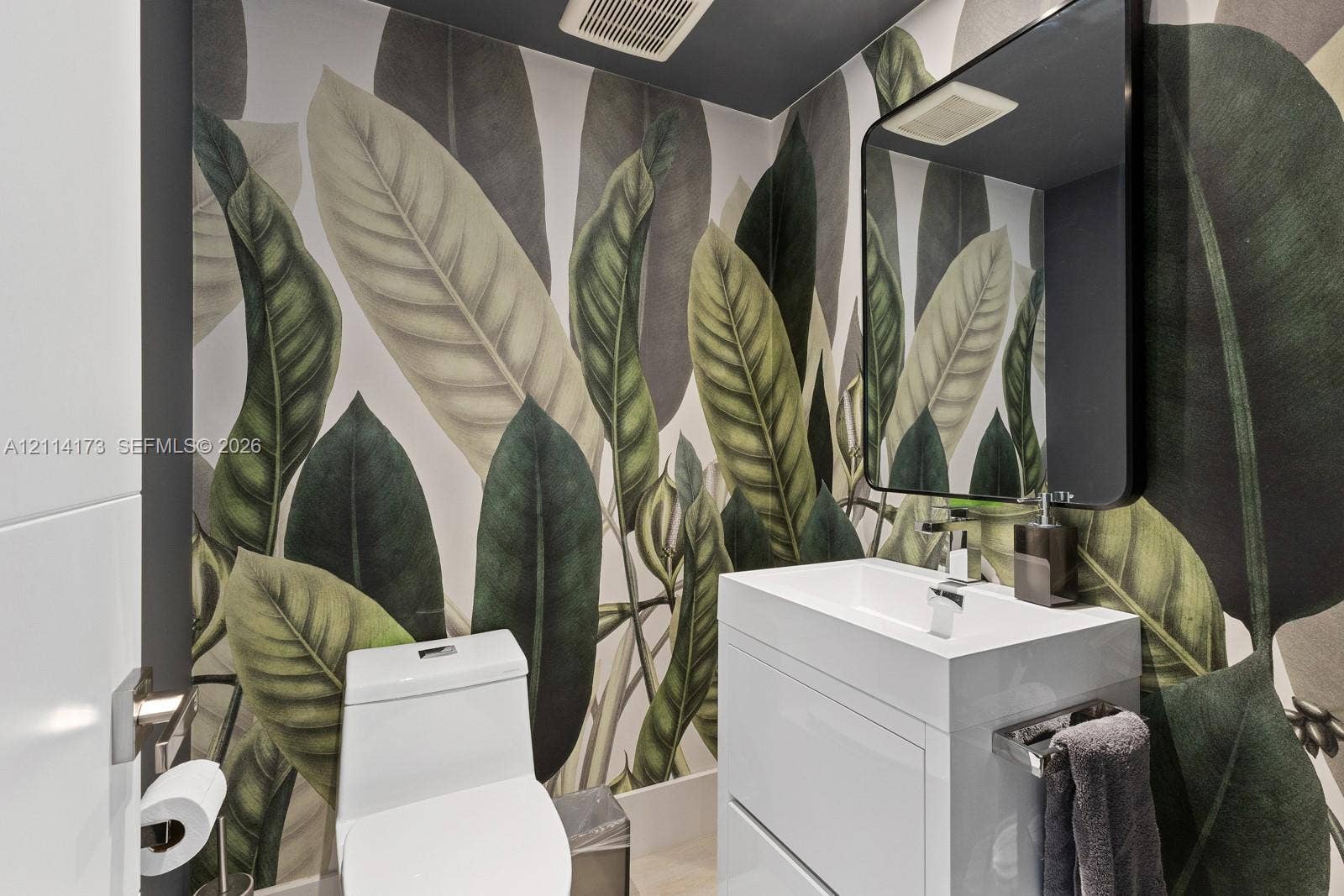 701 Brickell Key Boulevard, #1012, Miami, FL 33131 Botanical print wallcovering, white vanity cabinet with a rectangular basin, polished chrome faucet, and black-framed rectangular wall mirror