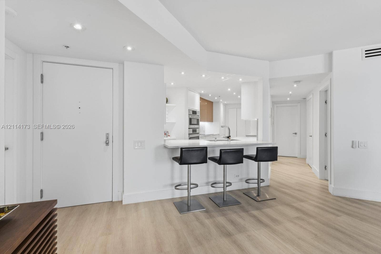 701 Brickell Key Boulevard, #1012, Miami, FL 33131 Kitchen featuring a breakfast bar with stone-surfaced countertop, built-in wall oven, recessed lighting, and wood-finish flooring
