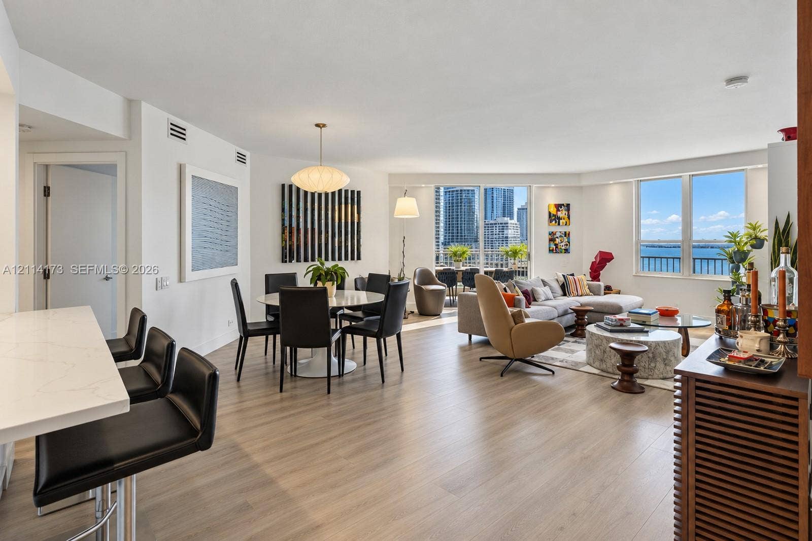 701 Brickell Key Boulevard, #1012, Miami, FL 33131 Open-concept main living area featuring light wood-finish flooring, quartz-surfaced kitchen island, recessed lighting, and expansive floor-to-ceiling windows with water and skyline scenery