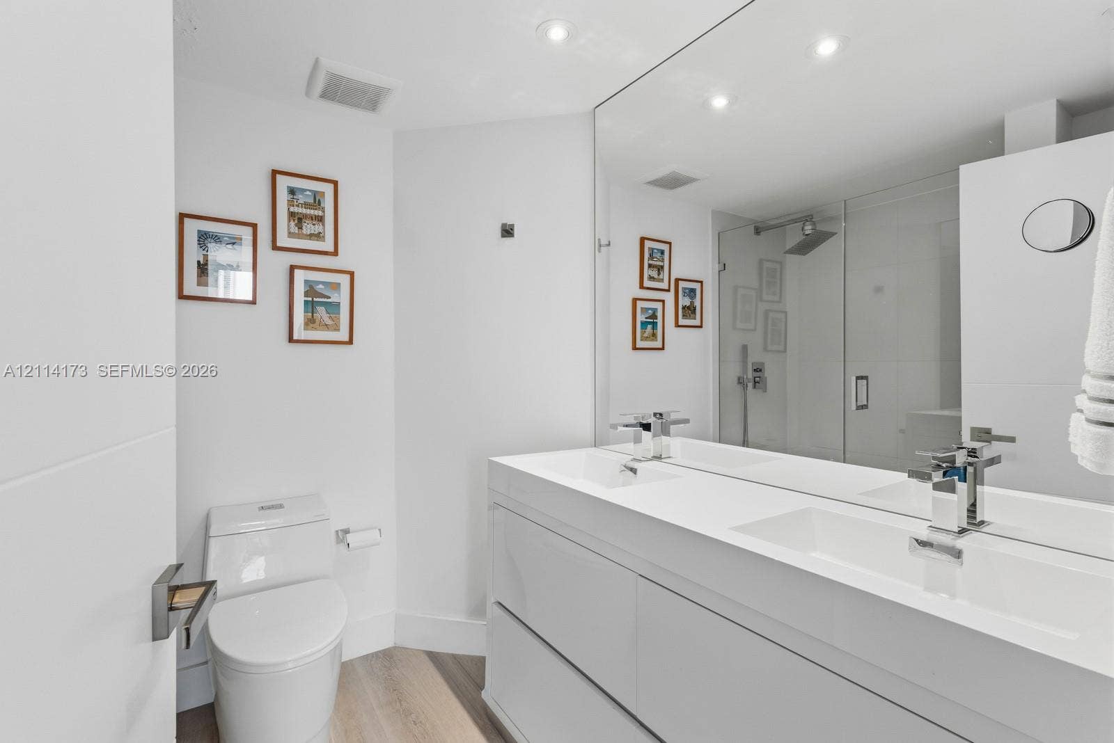 701 Brickell Key Boulevard, #1012, Miami, FL 33131 Dual-vanity cabinet with integrated rectangular sinks, expansive wall-to-wall mirror, glass-enclosed shower, and wood-finish flooring