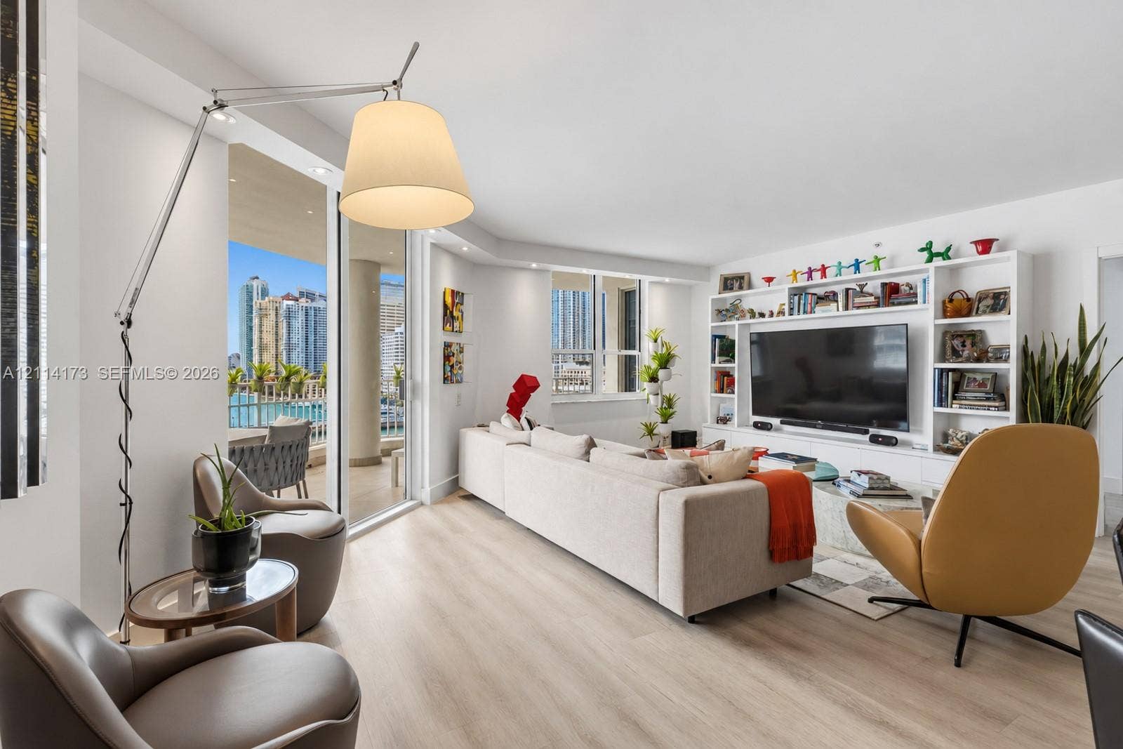 701 Brickell Key Boulevard, #1012, Miami, FL 33131 Open-concept living space featuring wood-finish flooring, floor-to-ceiling sliding glass doors, a large white built-in media center with integrated shelving, and recessed lighting
