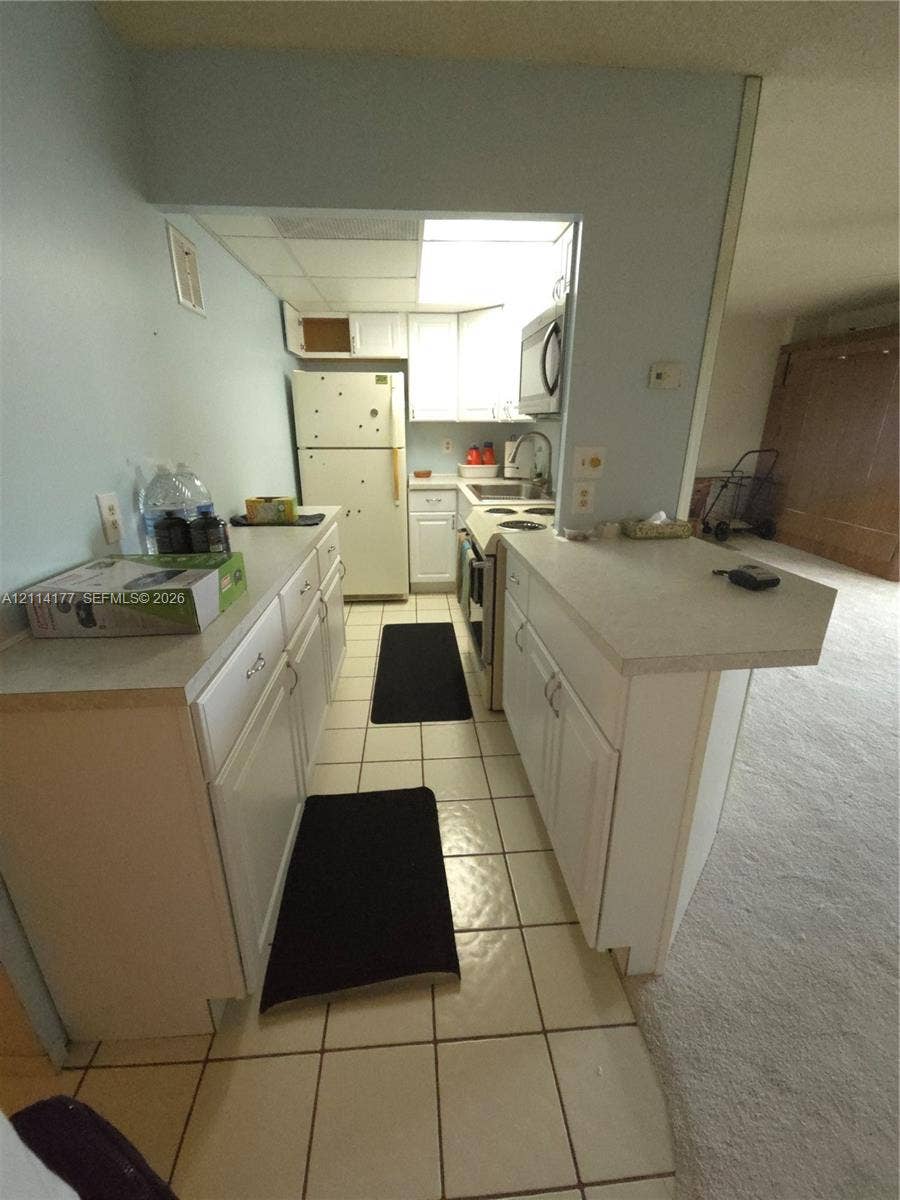 1731 SE 15th Street, #403, Fort Lauderdale, FL 33316 Kitchen featuring white cabinetry, solid-surface countertops, tile flooring, and integrated white appliances