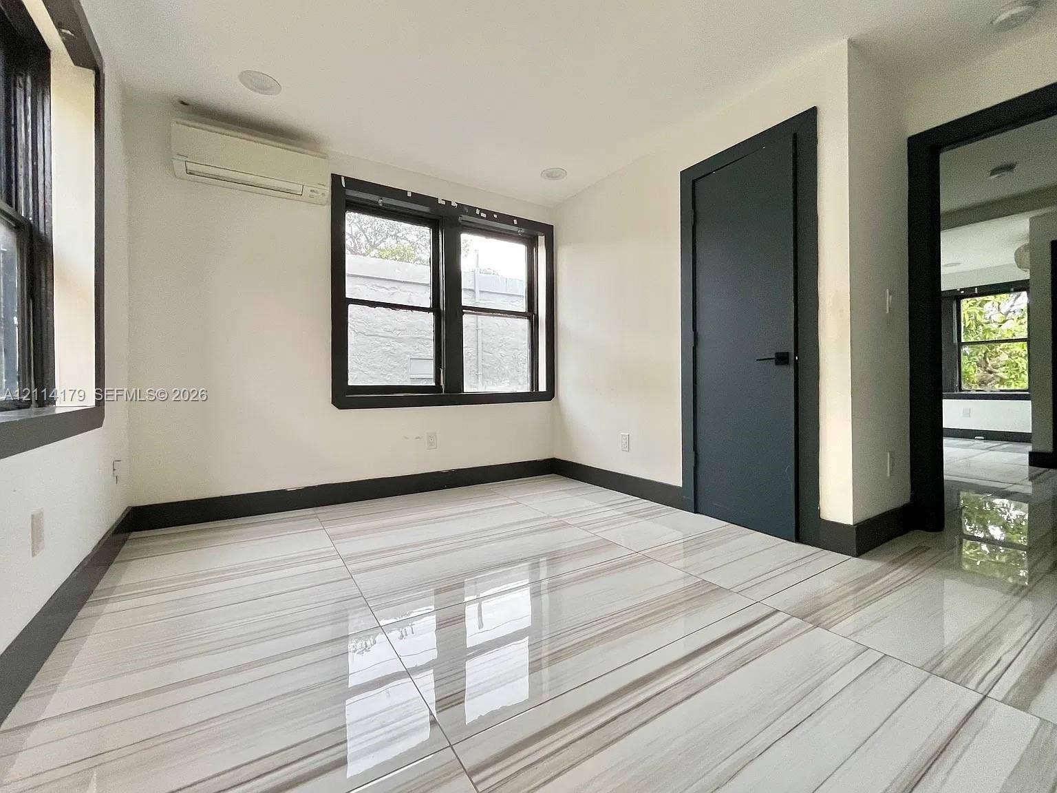 Large-format stone-look tile flooring with high-contrast veining, dark-framed dual-pane windows, recessed ceiling lighting, and a wall-mounted ductless climate control unit