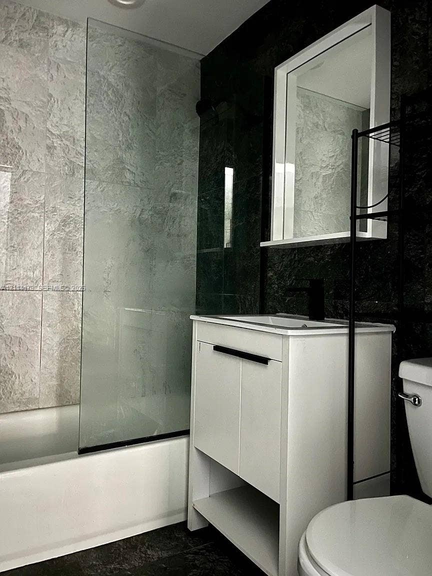 White vanity featuring integrated shelving and a dark-finish faucet, paired with a glass shower screen and dual-tone wall tile detailing