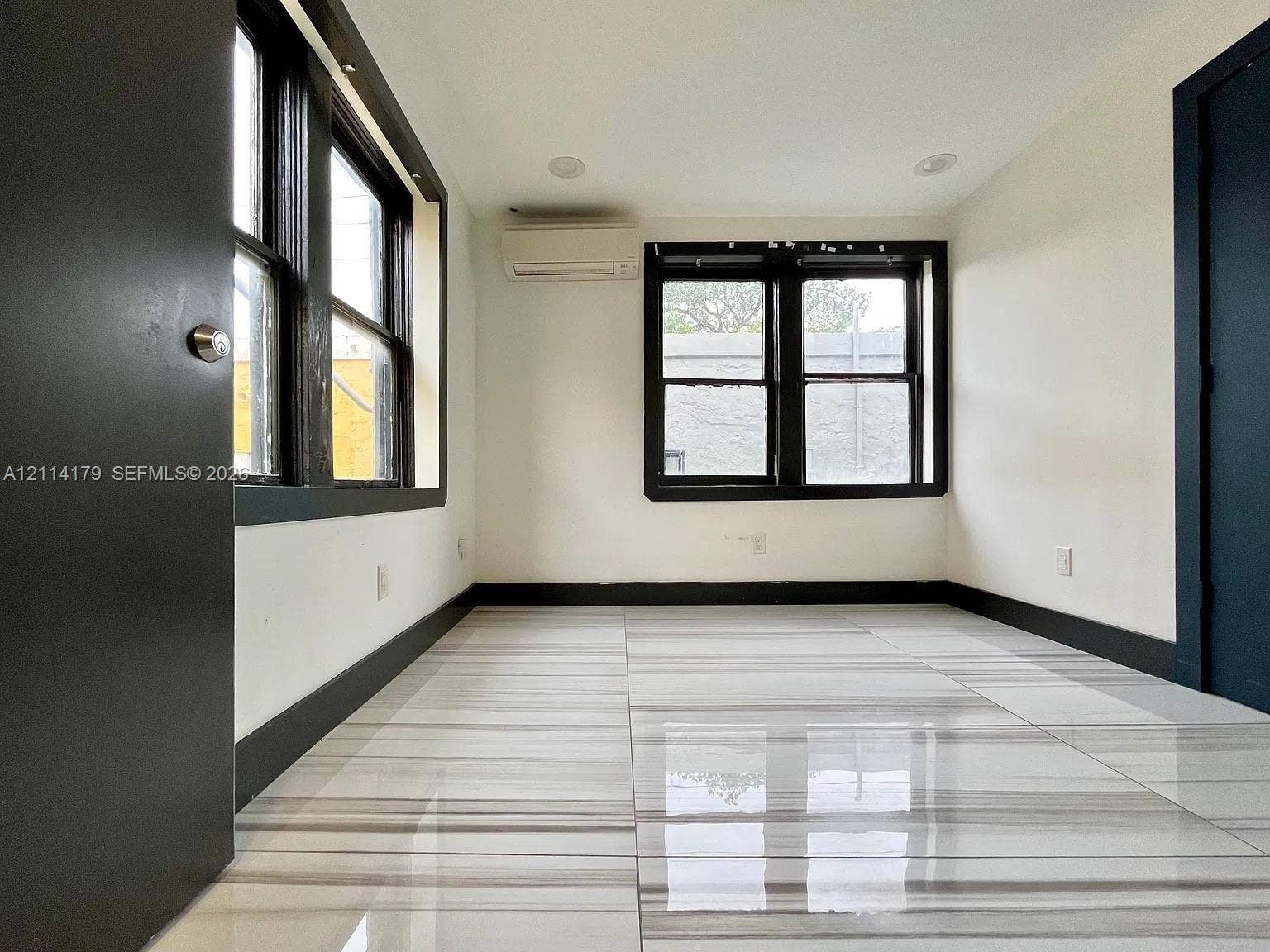Interior room featuring polished tile flooring with linear veining, dark-trimmed windows, recessed ceiling lighting, and a wall-mounted ductless climate control unit