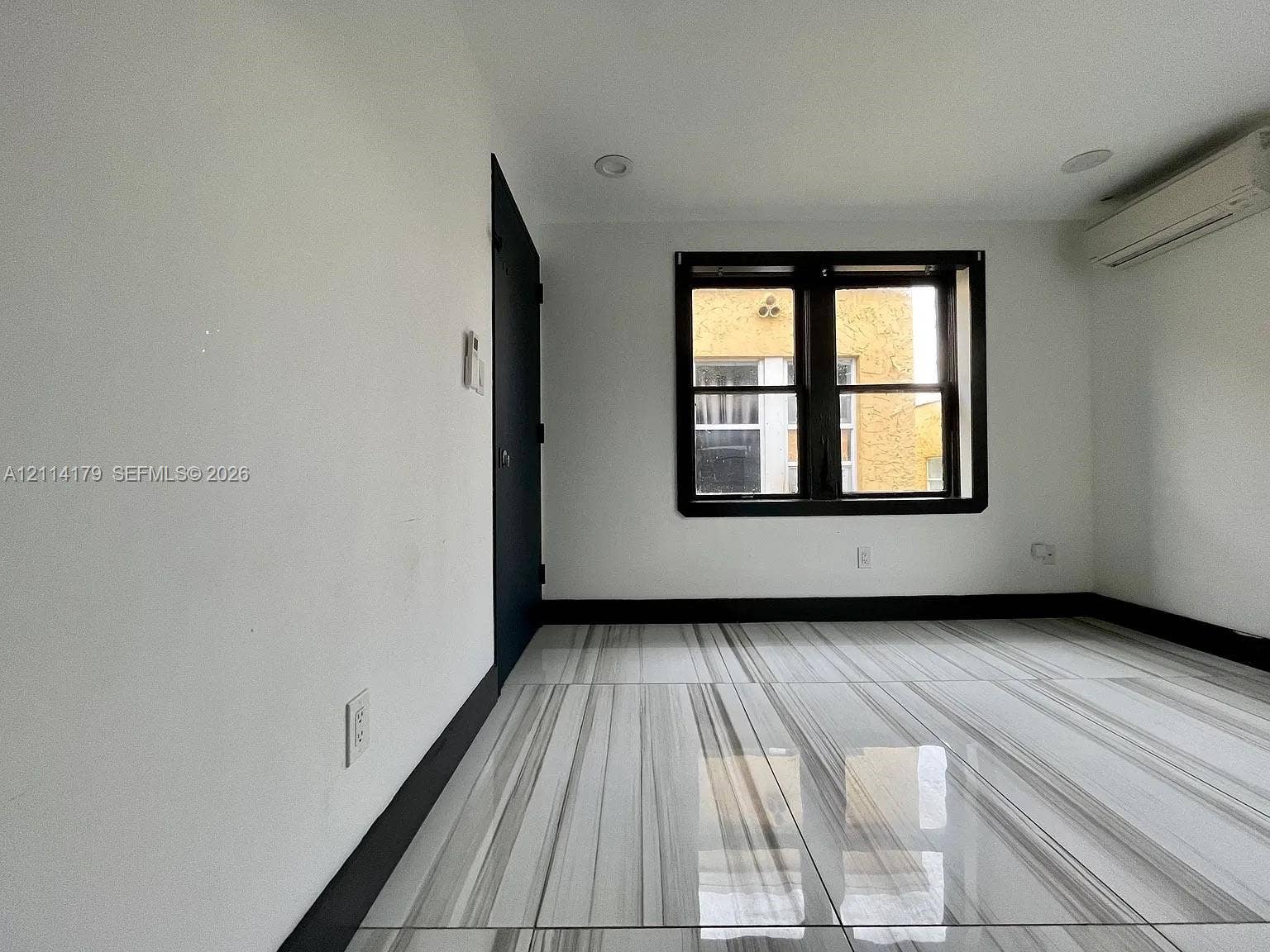 Interior room featuring large-format polished tile flooring, recessed ceiling lighting, a wall-mounted ductless HVAC unit, and a dark-framed window