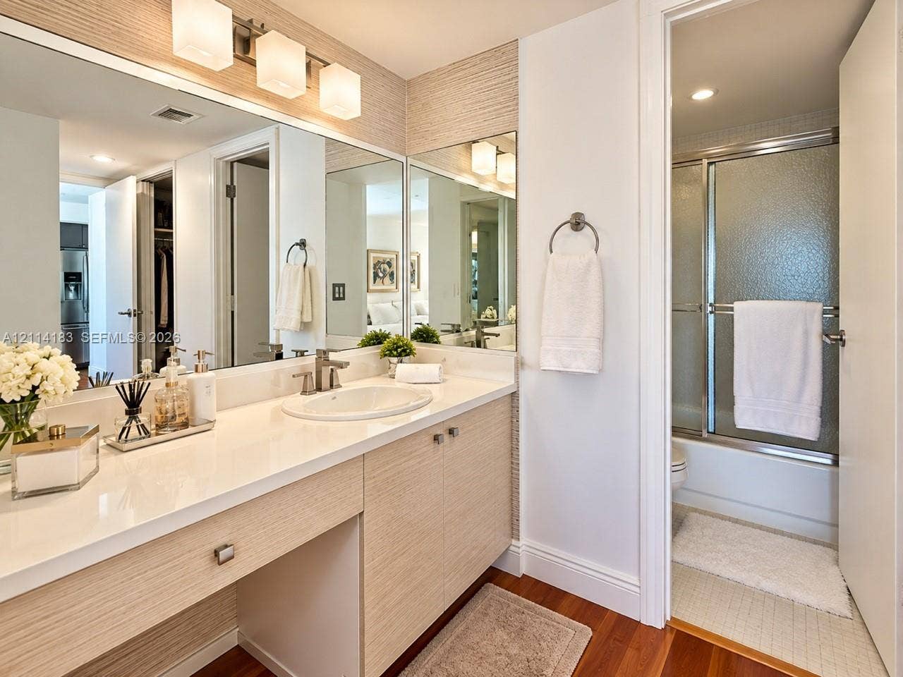 20379 W Country Club Drive, #938, Aventura, FL 33180 Bathroom featuring a vanity with wood-finish cabinetry, a crisp white countertop, integrated sink, and an expansive wall-to-wall mirror with triple-sconce lighting