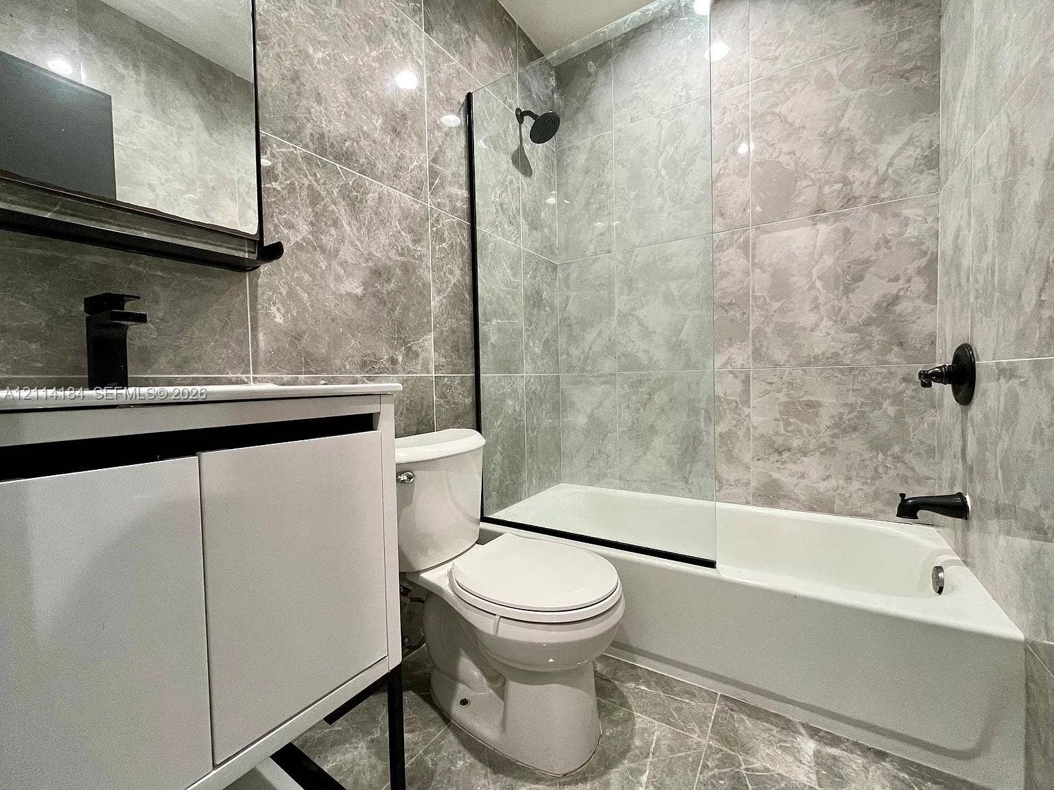 1614 Harrison Street, #1B, Hollywood, Hollywood, FL 33020 Bathroom featuring floor-to-ceiling stone-patterned wall tile, white vanity with black hardware, glass shower enclosure, and matte black plumbing fixtures