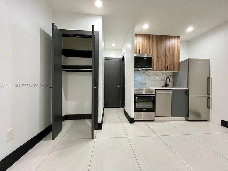 1614 Harrison Street, #1B, Hollywood, Hollywood, FL 33020 Kitchenette featuring dual-tone cabinetry, stainless steel appliances, stone-patterned backsplash, and large-format tile flooring, complete with a built-in storage closet