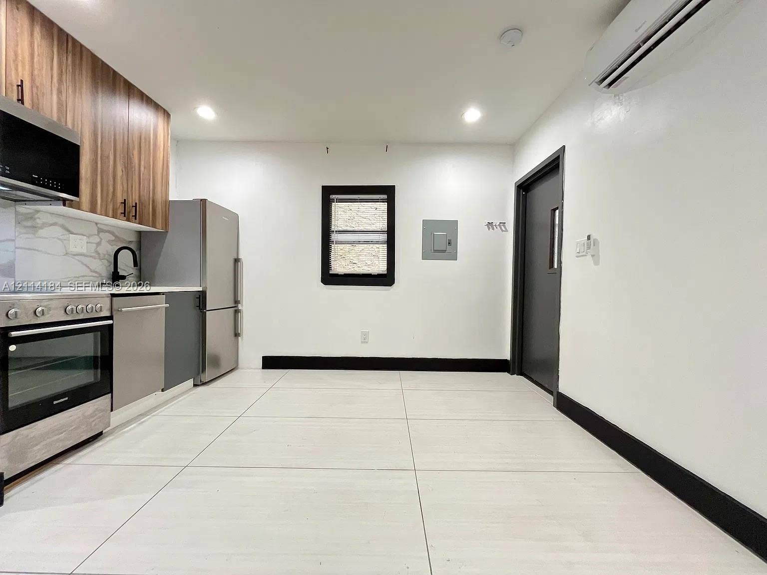 1614 Harrison Street, #1B, Hollywood, Hollywood, FL 33020 Kitchen featuring wood-finish cabinetry, stone-patterned backsplash, stainless steel appliances, large-format tile flooring, and a wall-mounted ductless heating and cooling unit
