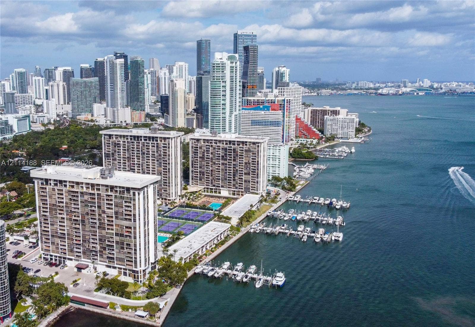 High-rise residential complex featuring multiple tennis courts, a swimming pool, and private deep-water boat slips along the waterfront