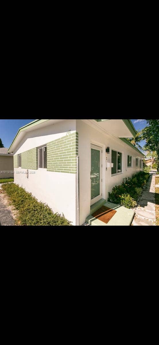 Exterior featuring white stucco finish, decorative brick accents, horizontal sliding windows, and a concrete entrance path