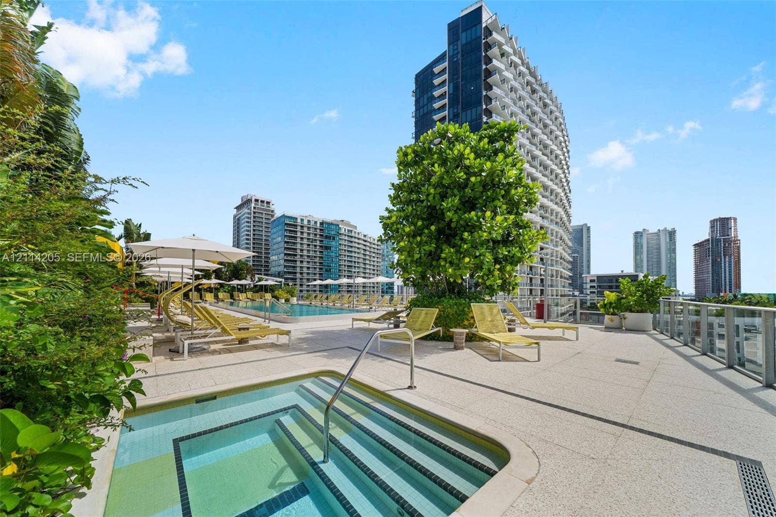 Outdoor terrace featuring an elevated spa, swimming pool, manicured greenery, and glass panel railing