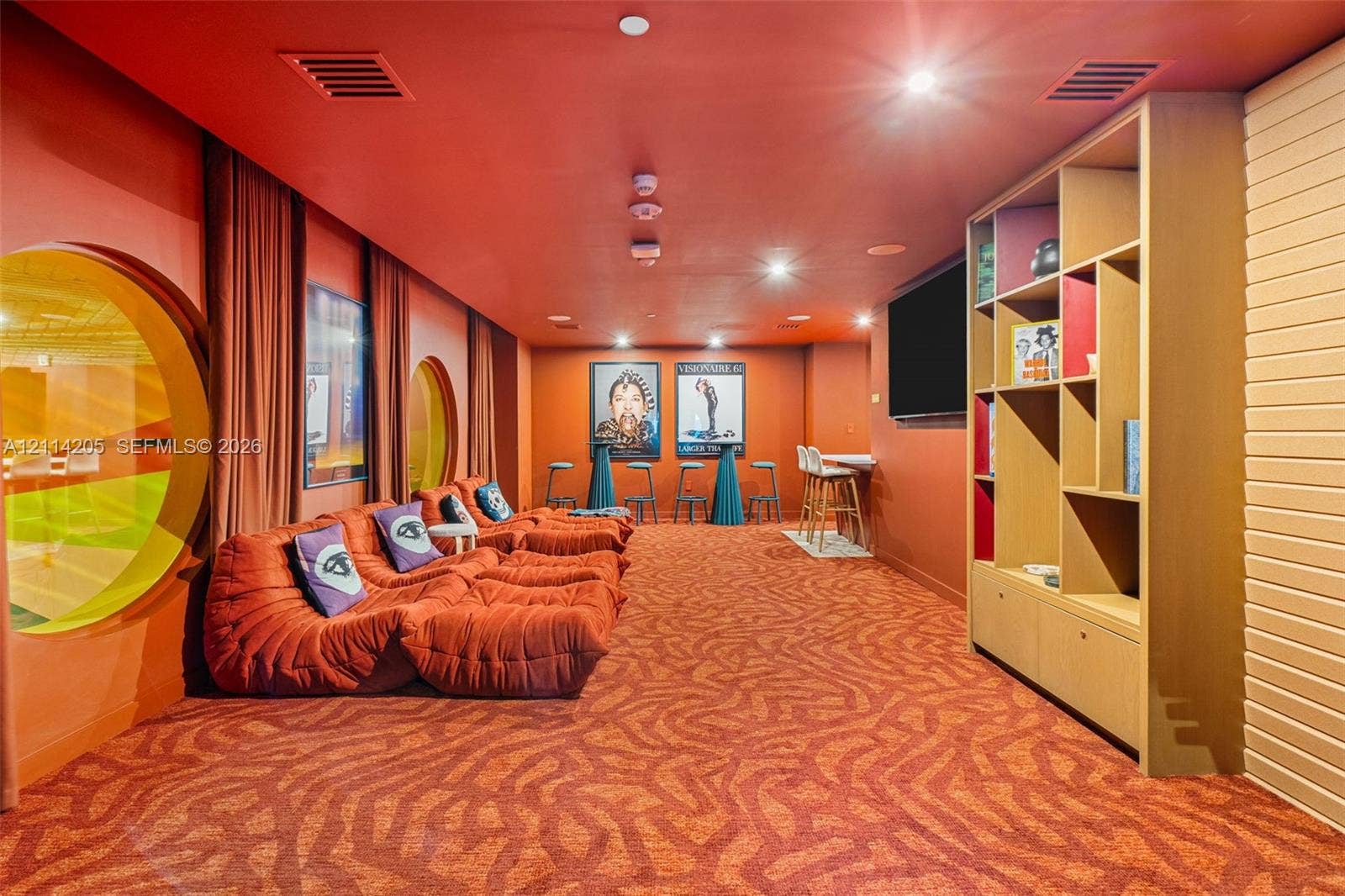 Custom media room featuring circular wall accents, built-in floor-to-ceiling shelving with cabinetry, patterned wall-to-wall carpeting, and recessed ceiling lighting
