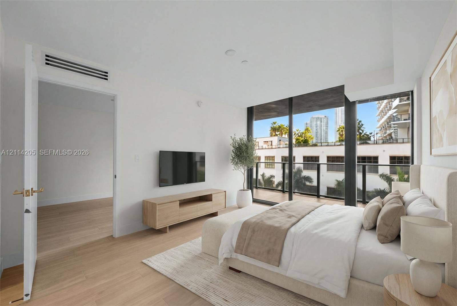 Floor-to-ceiling windows, wood-finish flooring, private balcony with black metal railing, and recessed ceiling lighting - staged