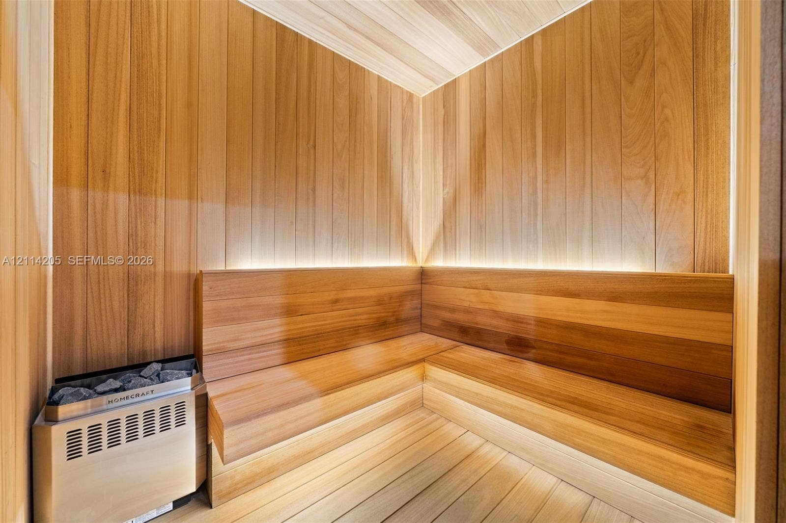 Sauna featuring wood-plank wall paneling, built-in tiered bench seating, recessed perimeter lighting, and a stainless steel heater unit
