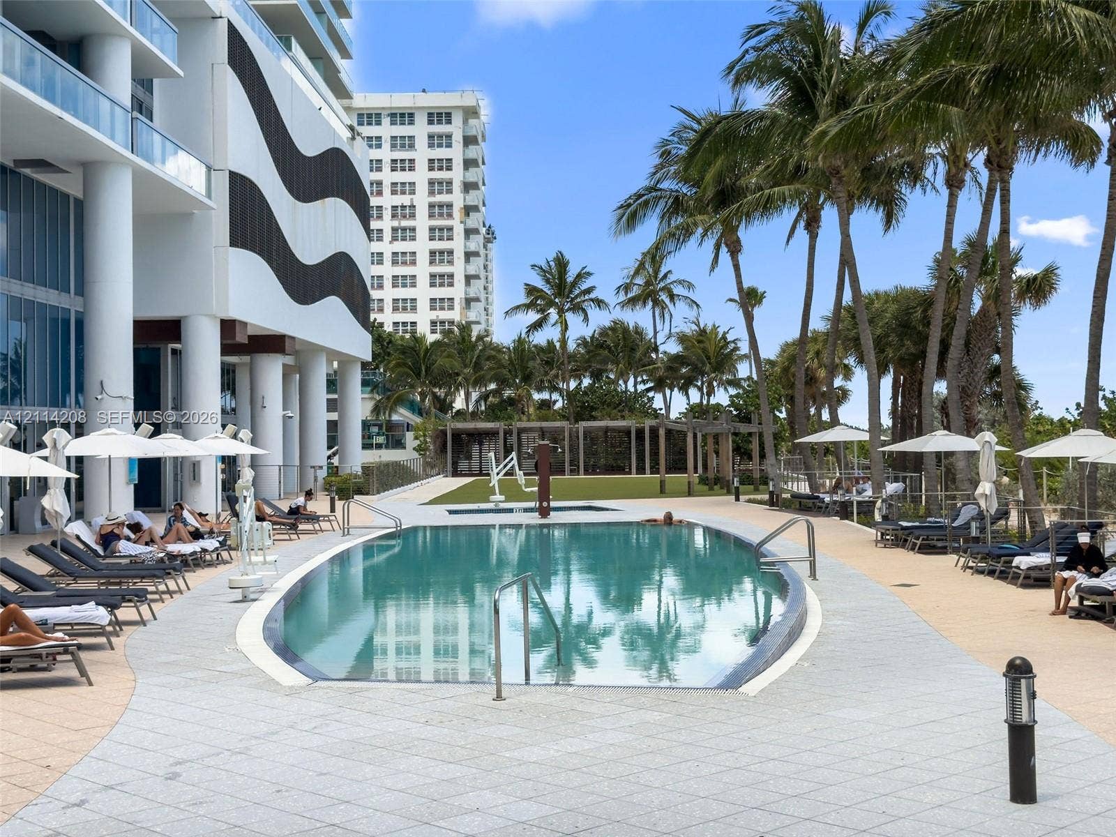 6801 Collins Avenue, #604, Miami Beach, FL 33141 Outdoor swimming pool featuring a curved concrete deck, metallic handrails, and surrounding mature palm trees