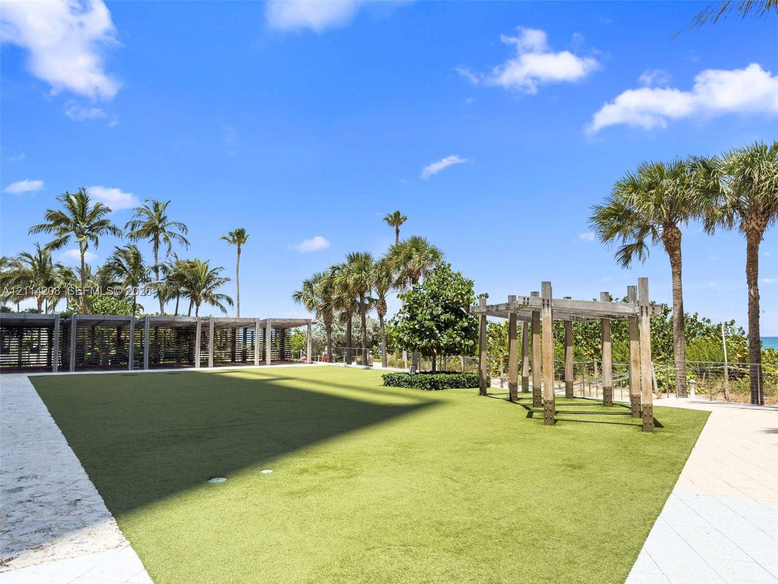 6801 Collins Avenue, #604, Miami Beach, FL 33141 Outdoor recreation area featuring artificial turf, wooden pergola structures, and paved walkways surrounded by mature palm trees