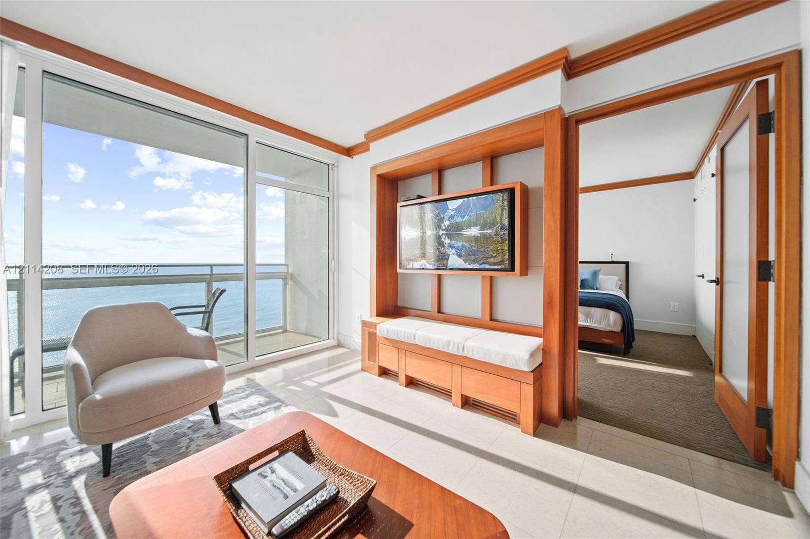 6801 Collins Avenue, #604, Miami Beach, FL 33141 Floor-to-ceiling glass sliding doors opening to a balcony, custom built-in wood shelving with integrated media console, polished tile flooring, and interior wood-framed doors