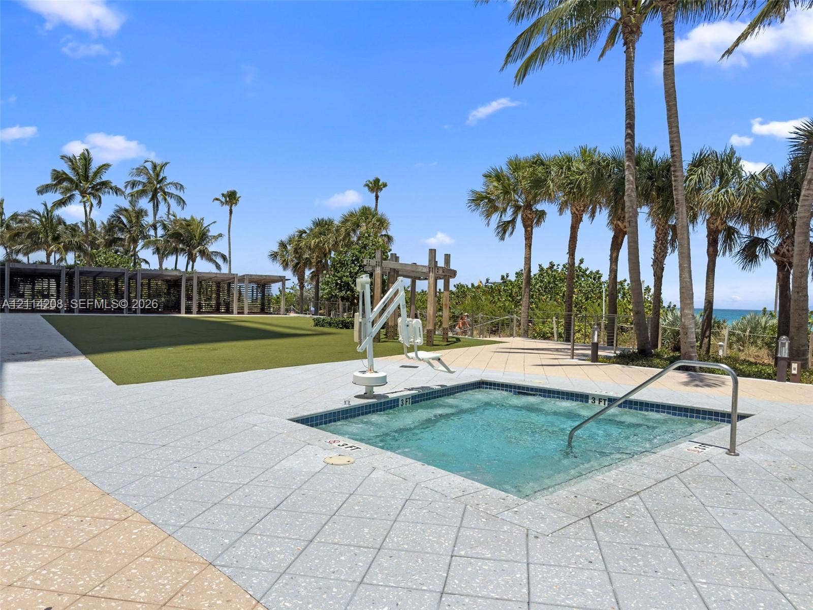 6801 Collins Avenue, #604, Miami Beach, FL 33141 In-ground spa featuring a tiled interior, metal handrails, and a dedicated pool lift, complemented by a large green turf area and paved sun deck