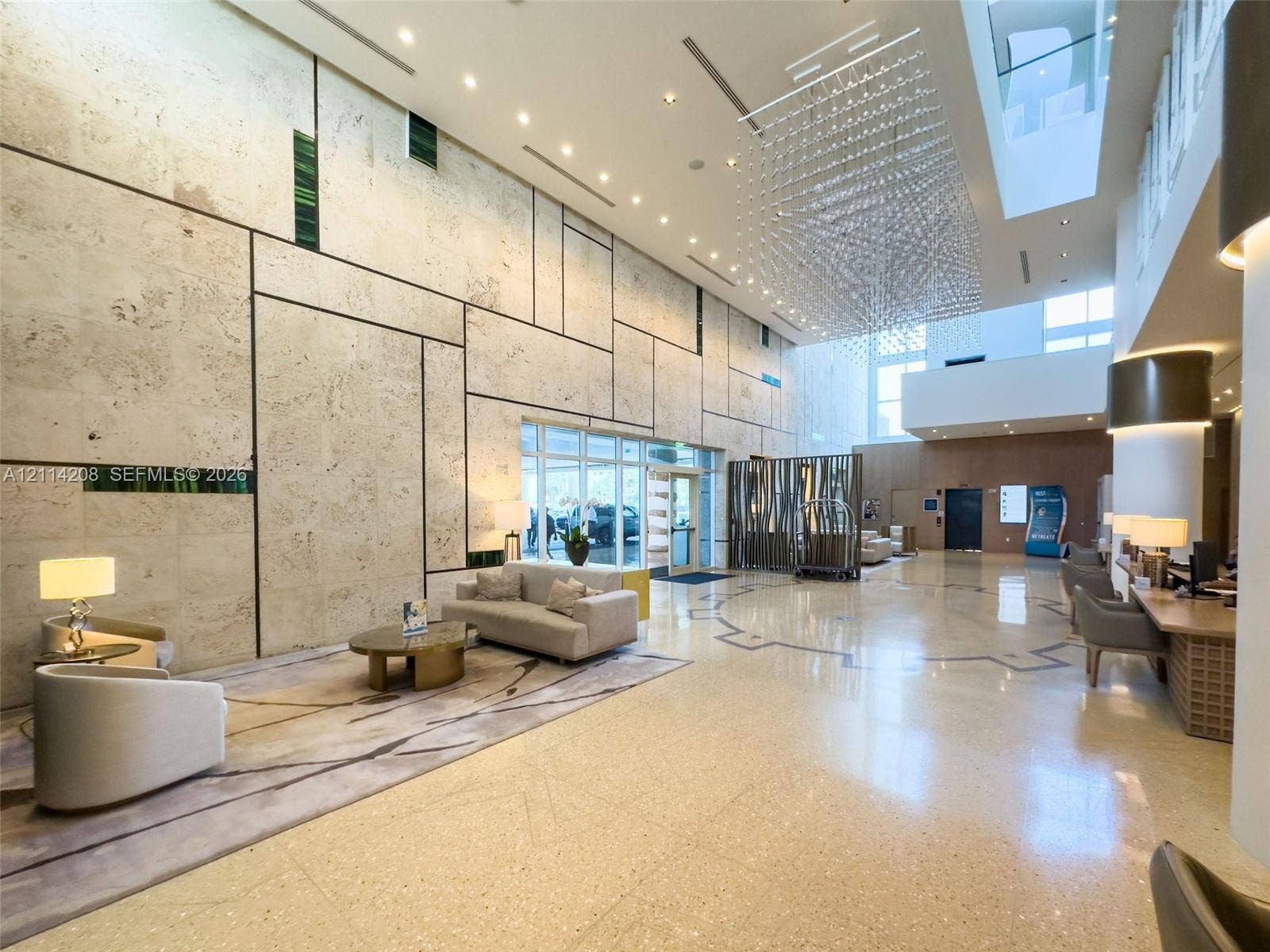 6801 Collins Avenue, #604, Miami Beach, FL 33141 Double-height lobby featuring expansive stone-tiled wall paneling, large-format polished flooring, a tiered crystal chandelier, and recessed lighting