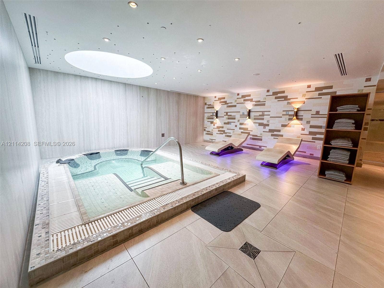 6801 Collins Avenue, #604, Miami Beach, FL 33141 Built-in sunken jetted tub featuring a stainless steel grab bar and tiled surround, recessed ceiling lighting with star-pattern accents, oval skylight, geometric textured wall tile, and large-format porcelain floor tiling