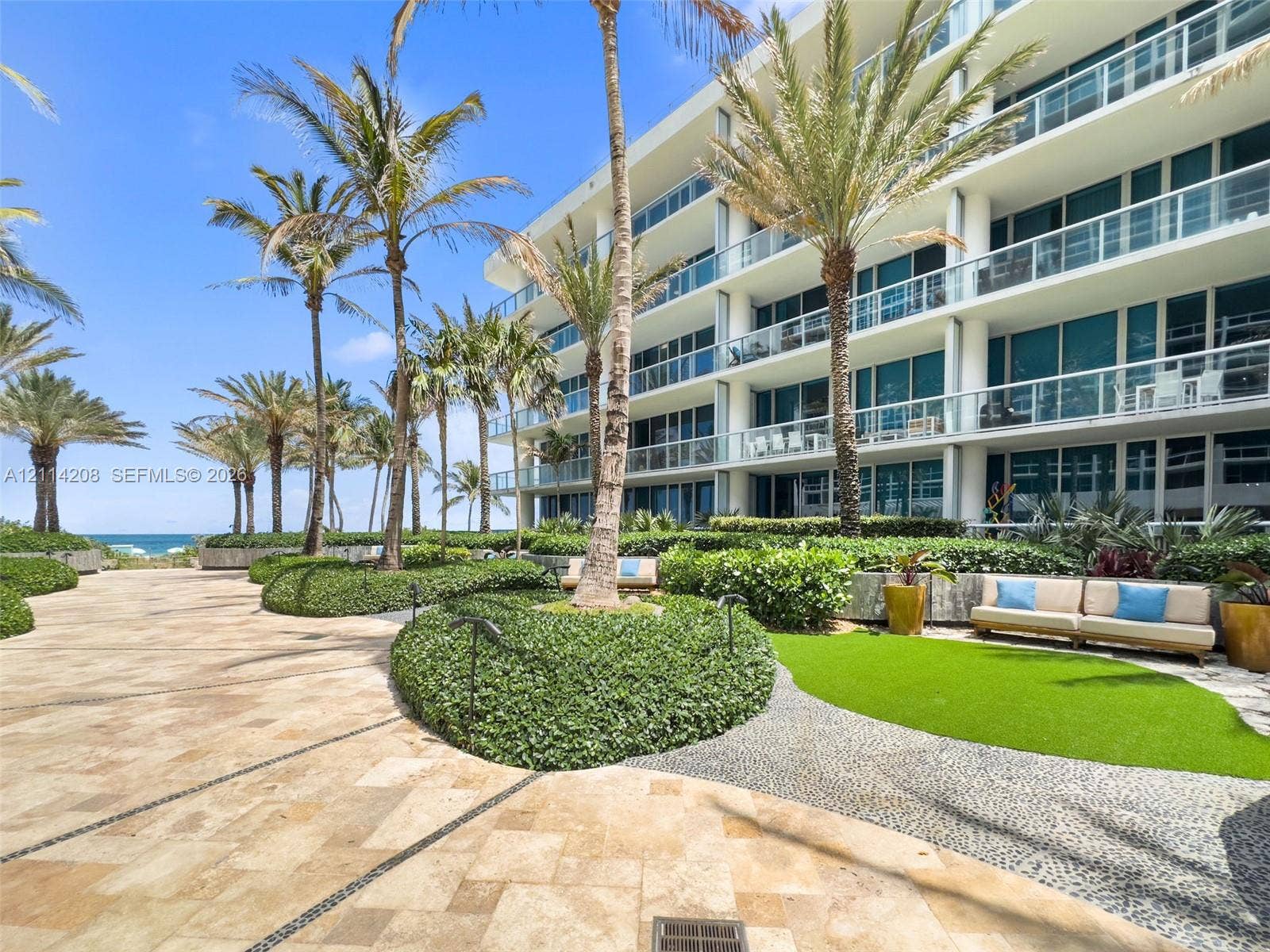 6801 Collins Avenue, #604, Miami Beach, FL 33141 Multi-story building featuring glass-railed balconies, stone-paved walkways, manicured landscaping, and mature palm trees